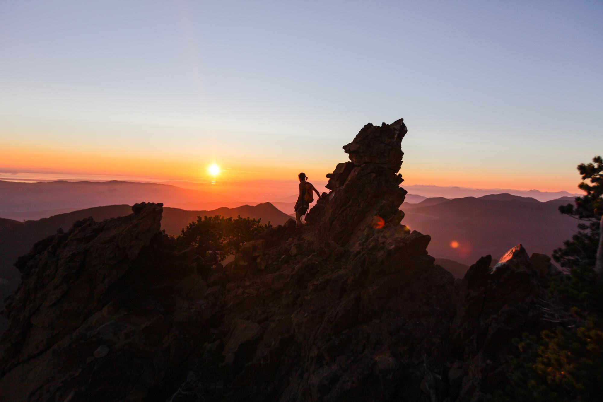 A person standing on a craggy peak viewing a sunset